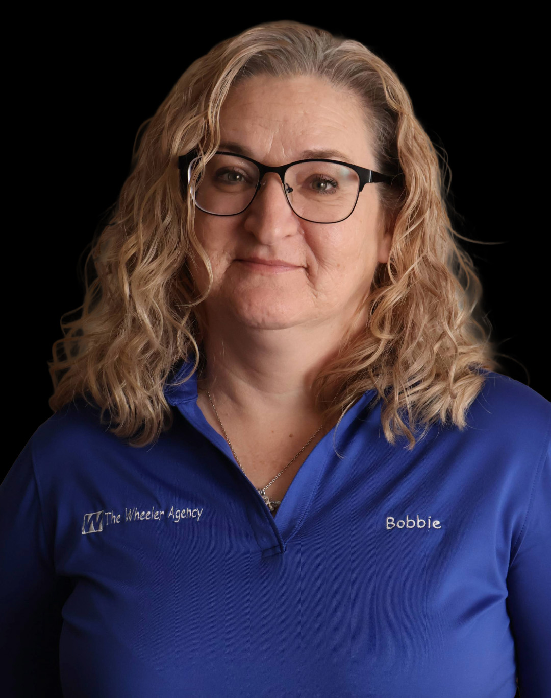 A woman with curly blonde hair, wearing a blue shirt, smiles confidently against a dark background.