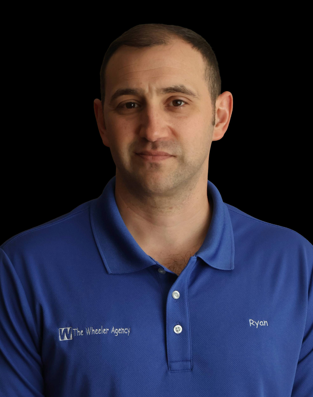 A man wearing a blue polo shirt stands against a black background, looking directly at the camera with a neutral expression.